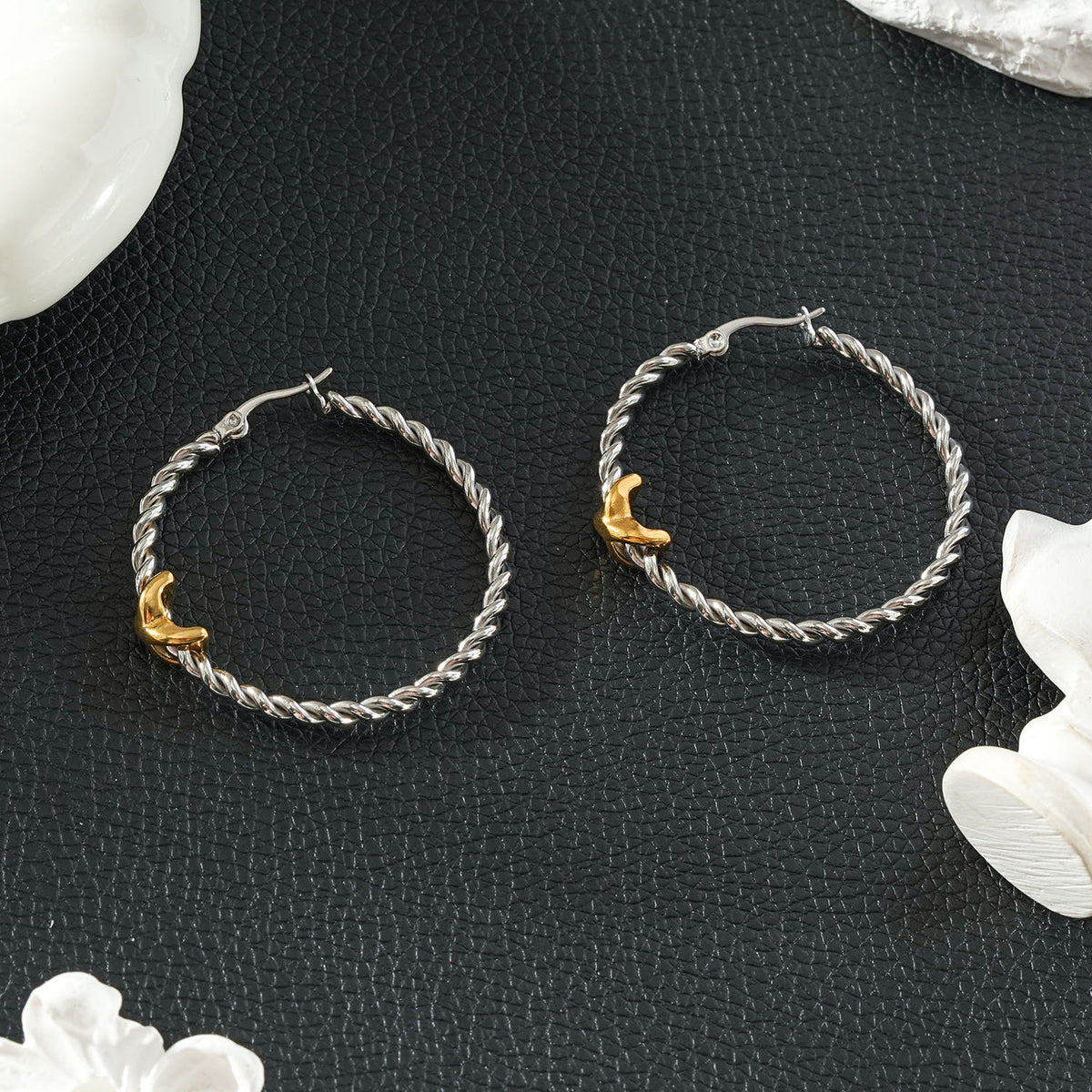 CIPRIANNA silver-tone rope twist hoop earrings with polished gold accents displayed on a textured black background.